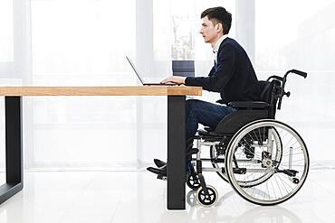 Side view young businessman sitting wheelchair using laptop new office