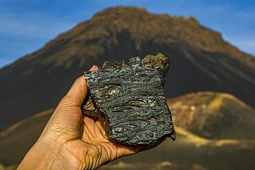 Hand holding piece of cold lava, vulcano in background. Fogo. Cabo Verde. Africa