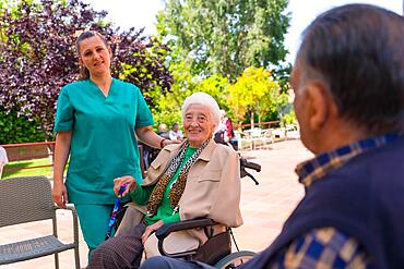 Portrait of an elderly woman with the nurse in the wheelchair in the garden of a nursing home or retirement home