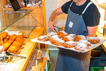 Unrecognizable baker of bakery in workshop workshop of artisan bakery and shop placing croissant and neapolitan