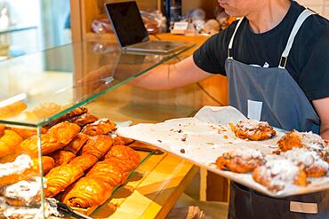 Unrecognizable baker of bakery in workshop workshop of artisan bakery and shop placing croissant and neapolitan