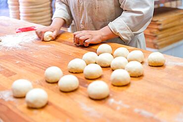 Woman breadmaker employee in the artisan bakery workshop preparing the dough in a circle