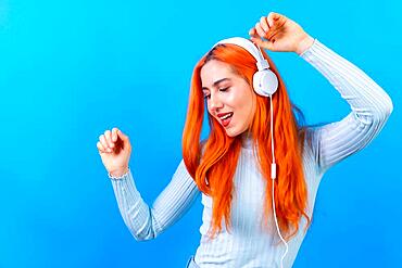 Redhead woman in studio photography smiling dancing on a blue background