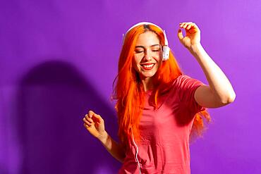 Redhead woman in studio photography dancing on a purple background, with a hard light