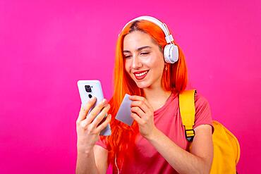 Redhead woman in studio photography pay online with mobile on a pink background