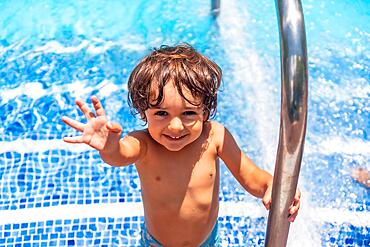 Two year old boy enjoying summer in a swimming pool, smiling on vacation from the water