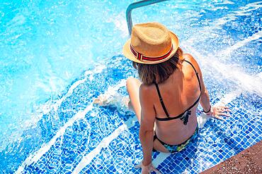 Woman in hat in pool at spa resort on vacation. Summer relaxing concept