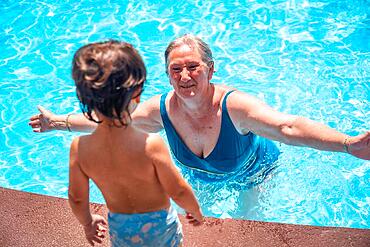 Mother and grandmother having fun with grandson in swimming pool on summer vacation, enjoying the water