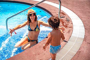 Mother and son in the pool on summer vacation, moment of love giving his mother a kiss