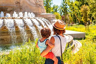 Mother with her son sightseeing at the fountain of the monument to Cervantes in the Spain square in the center of the capital of Madrid