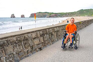 A disabled person in a wheelchair by the beach, having fun in summer