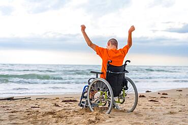 Disabled person on his back in a wheelchair on the beach with open arms enjoying the freedom