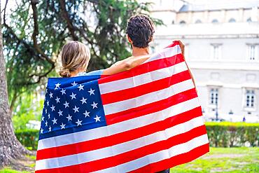 Couple in the city with usa flag, boy and girl on their backs. Patriots proud of their nation, independence day