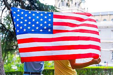 Couple in the city with usa flag, boy and girl on their backs. Patriots proud of their nation, independence day