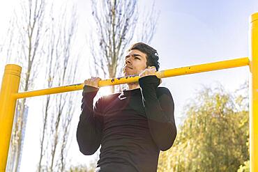 Attractive man doing pull-ups exercises on a crossbar in a public park