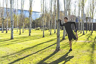 Attractive man leaning against a tree stretching his quadriceps. Copy man