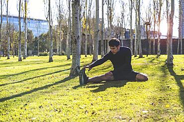 Sporty handsome man stretching legs after working out in city public park. Copy Space