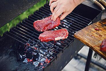 Unrecognizable man put raw strip steaks on hot grid of grill