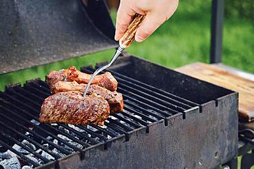 Unrecognizable man grilling steak outdoors. He turns meat with fork