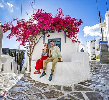 Young couple in love, white Cycladic house with blue door and pink bougainvillea, with sun star, picturesque alleys of Lefkes village, Paros, Cyclades, Greece, Europe