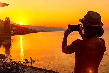 Silhouette of a woman taking a photo at sunset at Shkoder lake in Shiroka municipality, summer vacation. Albania