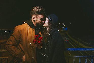 Young couple garland kissing dark street