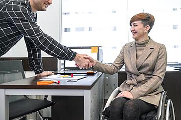 Confident businesswoman wheelchair shaking hands