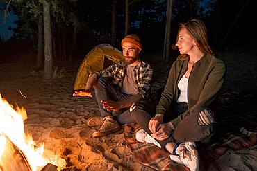 Couple warming up night by campfire