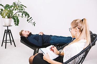 Female psychologist writing notes diary while patient lying couch clinic