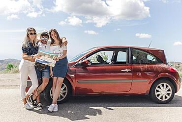 Three friends holding map standing near modern car road