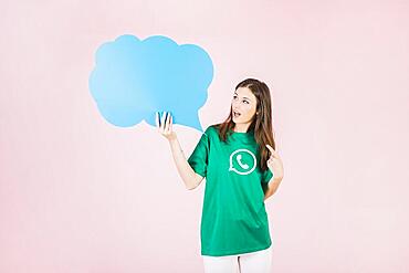 Young woman holding empty blue speech bubble pink background