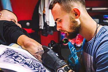 Adult man working with tattoo pen arm