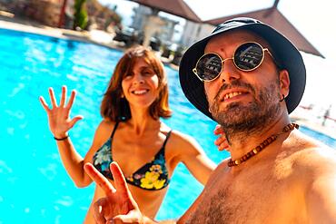 Tourist couple in the hotel pool in summer taking a selfie enjoying the vacation