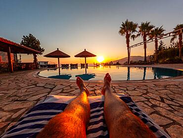 Feet of a man lying on a towel in a pool enjoying a sunset on summer vacation