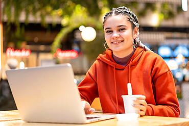 Alternative girl with white braids with a computer in a shopping center, making a video call with a hot coffee in her hands