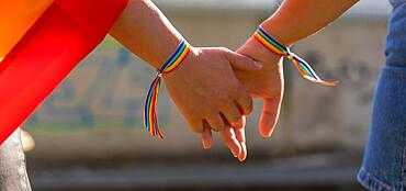 A closeup shot of two young Caucasian females holding hands with LGBT pride bracelets outdoors