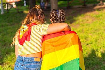 A closeup shot of two young Caucasian females holding LGBT pride flag outdoors