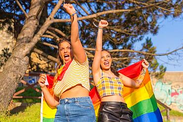 A closeup shot of two young Caucasian females holding LGBT pride flag outdoors