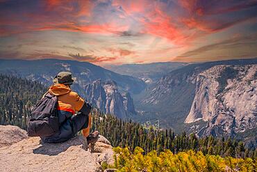 A young man on the trek sitting on the Sentinel Dome lookout in Yosemite National Park looking at El Capitan Mountain. United States