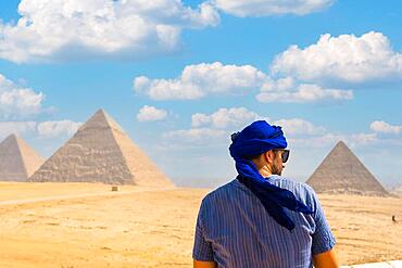 A young tourist wearing blue turban and sunglasses enjoying the Pyramids of Giza, the oldest Funerary monument in the world. In the city of Cairo, Egypt, Africa