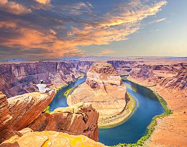 A young man sitting with a white shirt and green pants on Horseshoe Bend and the Colorado River in the background, Arizona. United States