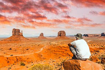 A young boy with white t-shirt sitting in the center of the photo on a stone in the Monument Valley National Park in the visitor center. Utah