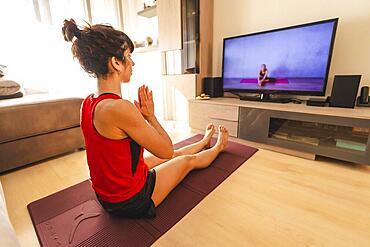 Yoga at home, a young woman meditating following the online instructions. In the coronavirus quarantine