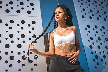 Young woman of black ethnicity with long braids and with tattoos, in the city enjoying the sun