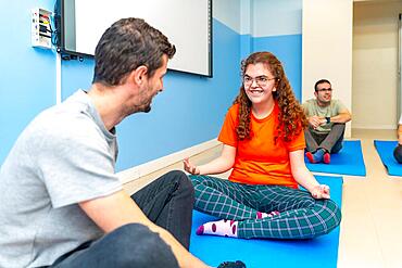 Yoga instructor and disabled woman talking while practicing yoga sitting on a mat with other people