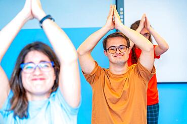 Happy group of disabled people raising arms practicing yoga in the gym