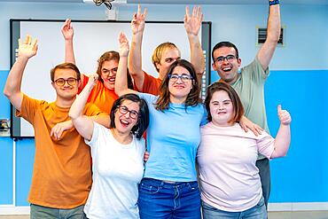 Happy people with special needs posing after gymnastic class laughing at the camera and raising hands