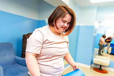 Woman with down syndrome pick up a yoga mat after exercising in a gym