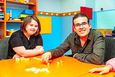 Two people with special needs distracted playing board games sitting on a table in a day centre