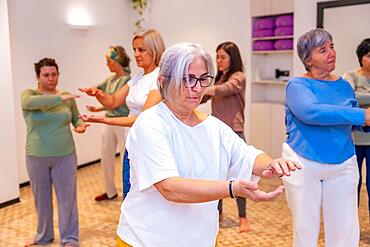 Mature adult caucasian concentrated women exercising in pairs during Qi gong class